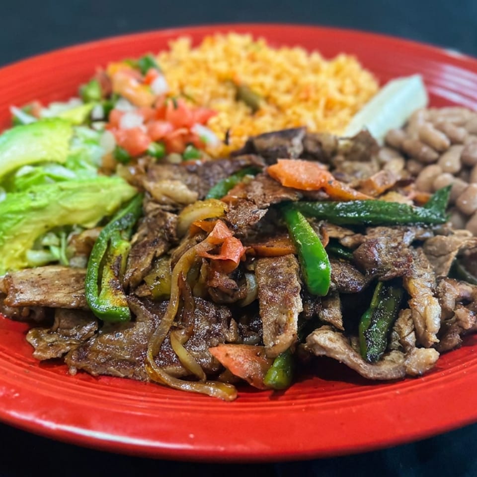 Red plate of grilled beef and vegetables with rice, beans, avocado, lettuce, and pico de gallo.