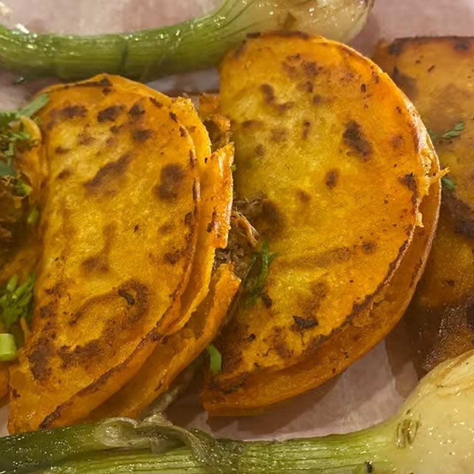 Four golden, grilled folded tacos topped with chopped herbs, served with roasted green onions and garlic.
