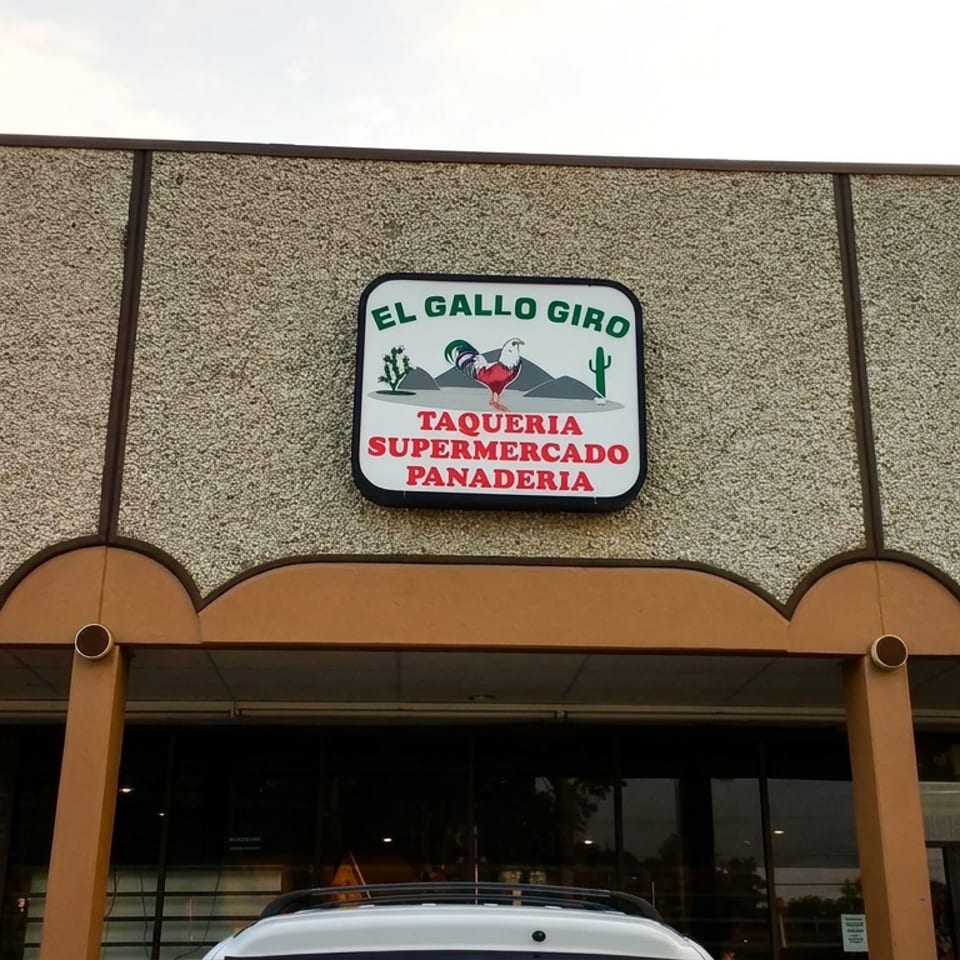Exterior of El Gallo Giro taqueria, supermercado, and panaderia with a colorful rooster sign above the storefront.